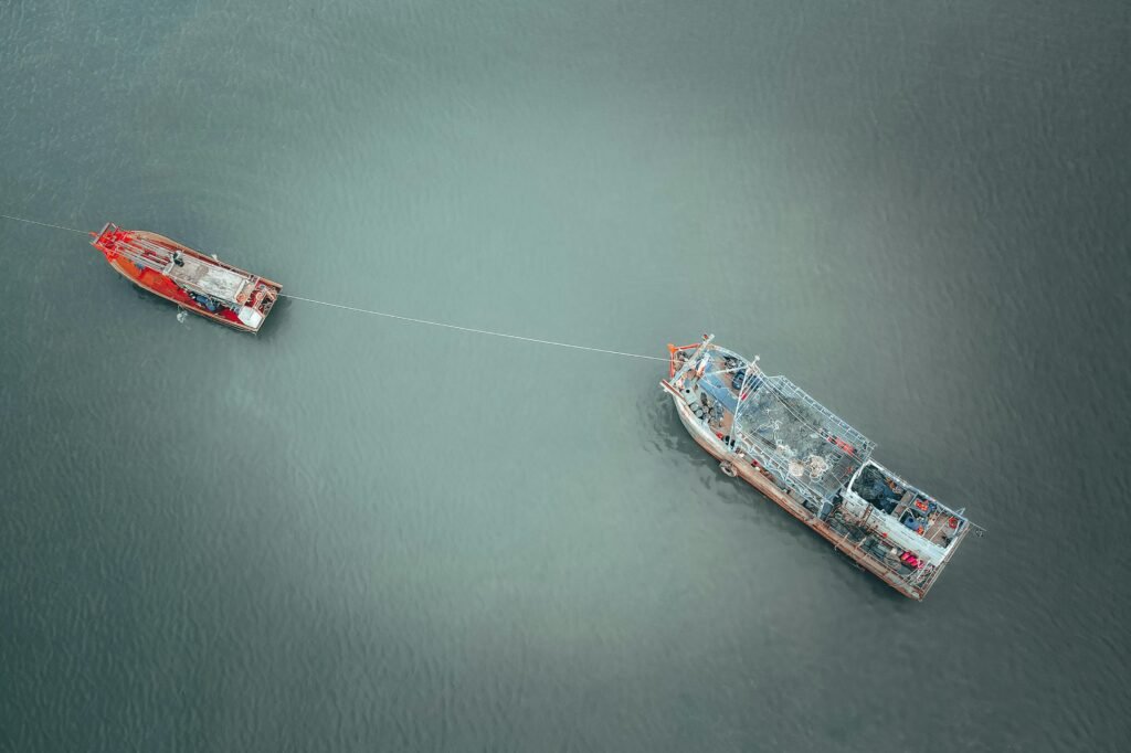 Aerial shot of fishing boats connected by rope in serene waters, showcasing tranquility.