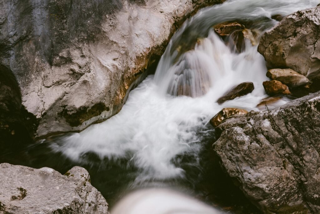 A tranquil stream flows over rocks, creating a small waterfall in a natural setting.
