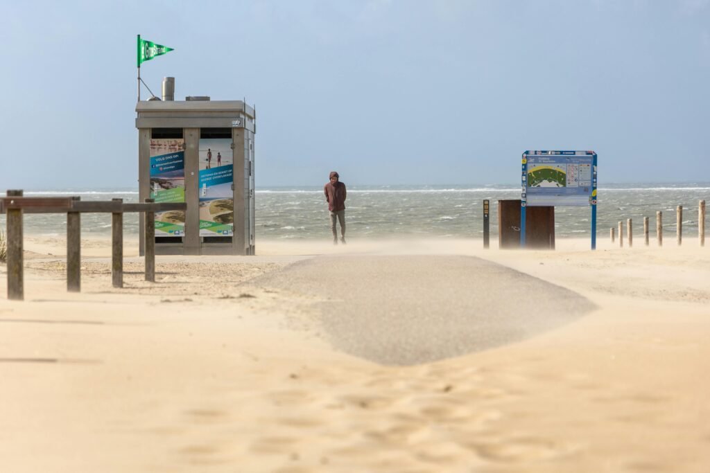 Windswept beach scene with a lone figure walking along a sandy path in a coastal area