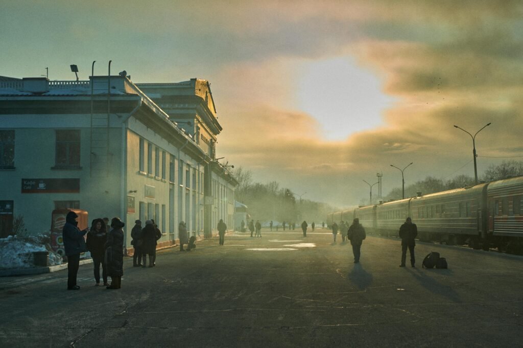 A scenic winter sunset at Komsomolsk-on-Amur train station with people and a passenger train.